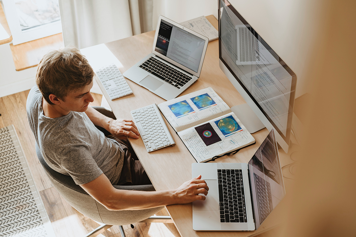 man in front of large computer monitor and 2 laptops